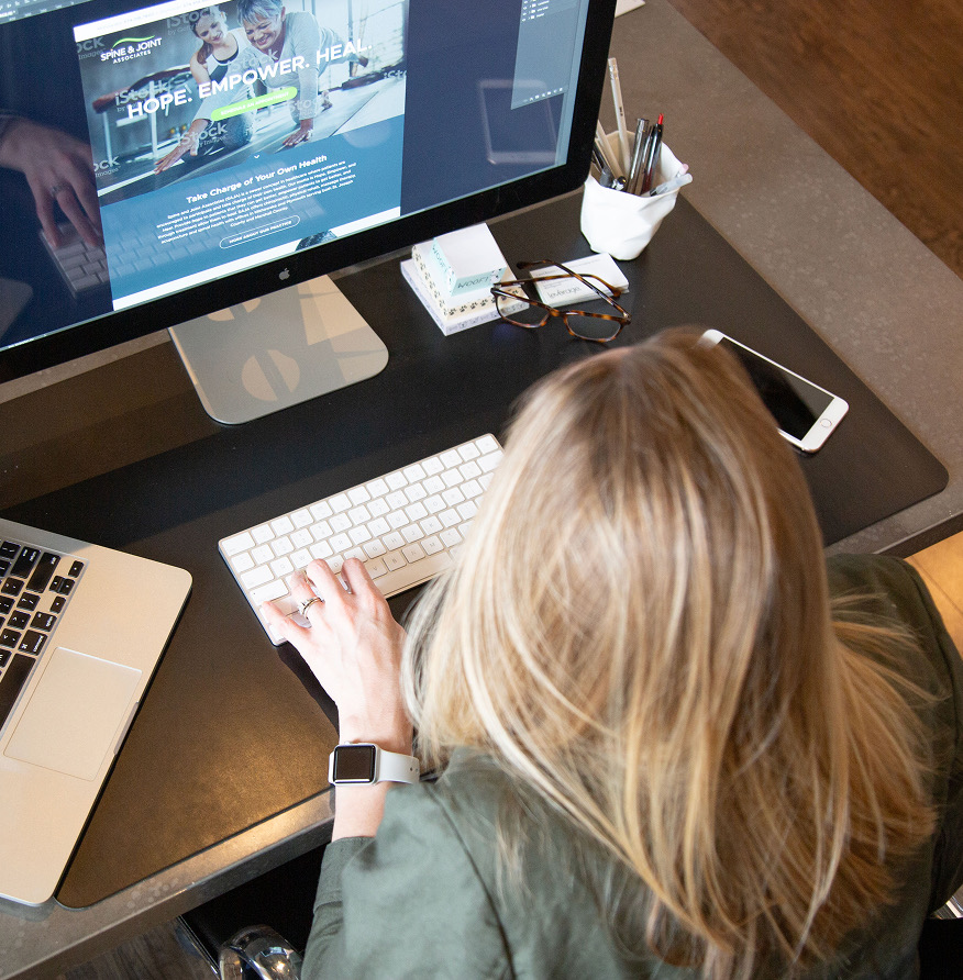 Overhead view of a woman at a desk designing a healthcare website on a large monitor.