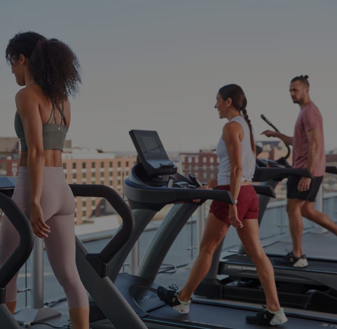 People walking on treadmills at a rooftop gym.