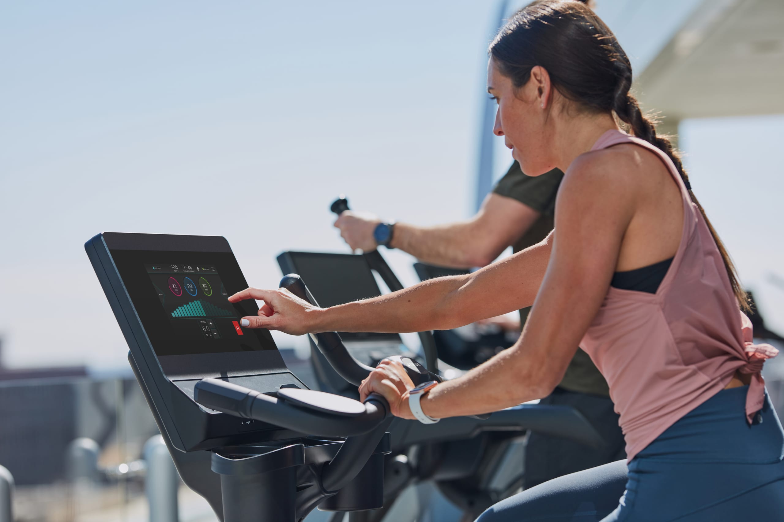 People walking on treadmills at a rooftop fitness center overlooking the city.